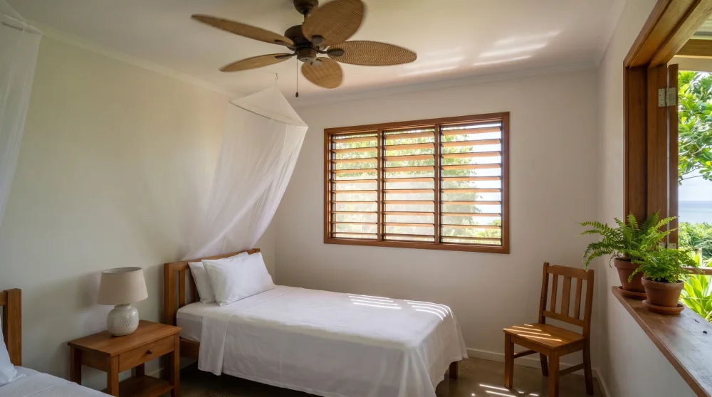Interior of a simple clean guesthouse room in Funafuti, Tuvalu with bed, ceiling fan and louvered window